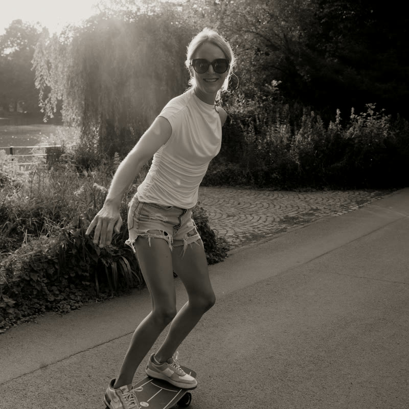 Alina f&auml;hrt l&auml;chelnd Surfskate im abendlichen Park